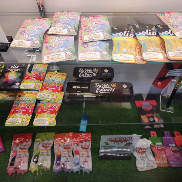 Display case showcasing colorful cannabis cartridges and extracts, featuring brands like Olio and Dobbie Extracts on a grassy background.