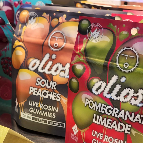 Two colorful packages of Olio's live rosin gummies, featuring Sour Peaches and Pomegranate Limeade flavors, labeled as vegan-friendly.